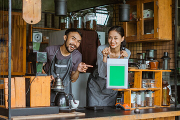 a couple of barista pointing on the digital tablet with green screen while standing inside the bar desk