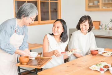 家のダイニングで家族団欒して食事する子供と夫婦・親子・三世代家族（二世帯住宅・帰省・里帰り）
