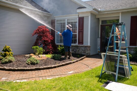 A man using a power washer to clean the windows and front of a house