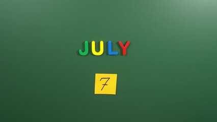 Hand sticking a sticker 7 July calendar day on school board. 7 date of July. Seventh day of July. 7th date number. 7 day calendar. Seven date. World Chocolate, Global Forgiveness