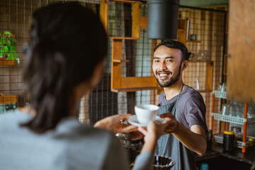 the male barista smiling while giving the cup of coffee to the female barista