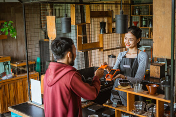 the female barista smiling while receiving the credit card from the customer during the transaction on the cashier desk