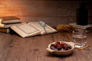 Many Date Palms are on bowls, plates, a cup of water, and the Quran, islamic style lamps on wooden tables, to wait for the time of Iftar, with the concept of ramadan Muslims around the world.