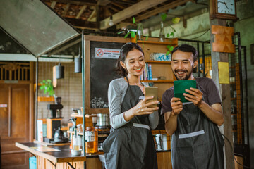 female barista smiling and looking at the phone while standing beside the male barista that holding the deposit book