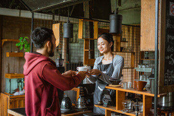 the male customer receiving the cup of coffee from the female barista that standing inside the bar desk