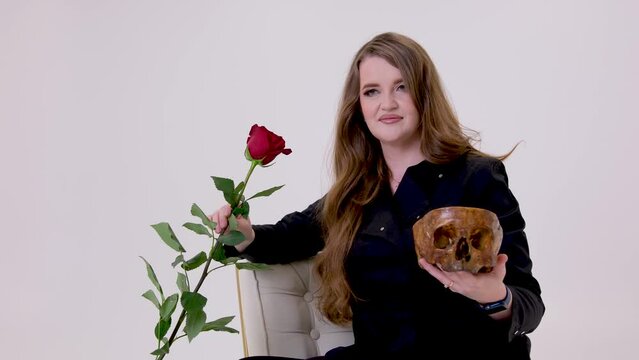 woman in black holds a red rose in one hand in the other hand a human skull insidious woman vampire gorgeous hair on a white background Lost love studio fatal girl fatal