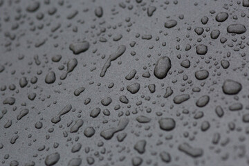 Tiny raindrops falling on a black metal surface