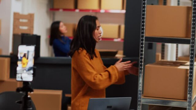 Depot employee filming marketing video on phone, using social media streaming platform for advertising. Young female employee recording merchandise promotion for online ad campaign.