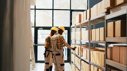 Team of employees working on logistics with scanner and list of goods, planning distribution with merchandise inventory. Two men scanning retail store products on racks in depot. Handheld shot.