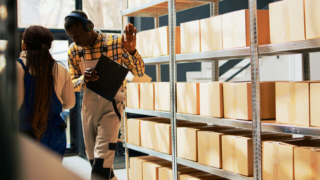 Storage room employee dancing and listening to music, having fun with dance moves in warehouse. Male worker preparing merchandise or supplies in containers, cardboard boxes. Tripod shot.