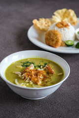 soto ayam or chicken yellow soup in white ceramic bowl, usually served with cooked rice, and potatoes cake