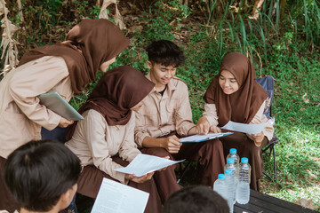 Scout members work on assignment papers together while sitting together in nature