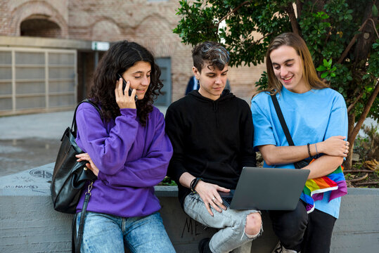 Young diverse people with lgbt rainbow flag using laptop and mobile outdoors.
