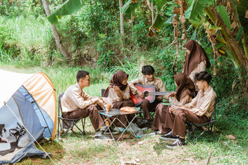 group of young scouts singing with a guitar while gathering beside a tent in nature