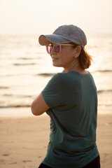 portrait of asian woman wearing jeans cap standing at sea beach against beautiful sunset light