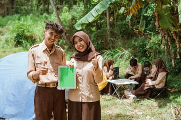 boy scouts and girl scouts smiling with thumbs up showing digital tablet screen with scout camping background