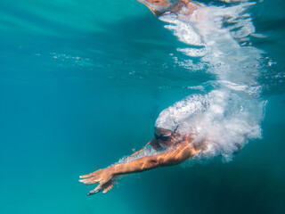 A talented female swimmer dives into a full-size tournament pool to train or compete. This stunning wide-angle underwater photo captures the grace and power of this athlete in action.