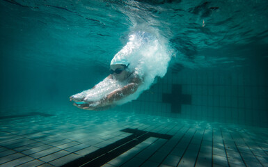 A talented female swimmer dives into a full-size tournament pool to train or compete. This stunning wide-angle underwater photo captures the grace and power of this athlete in action.