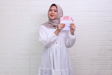 Beautiful Asian muslim woman wearing hijab showing some money on envelope as eid al fitr present. 