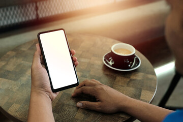 Mockup image of a man holding mobile phone with blank white screen with coffee cup on wooden table