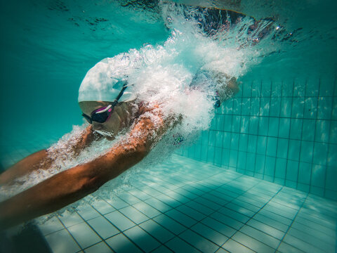 A talented female swimmer dives into a full-size tournament pool to train or compete. This stunning wide-angle underwater photo captures the grace and power of this athlete in action.