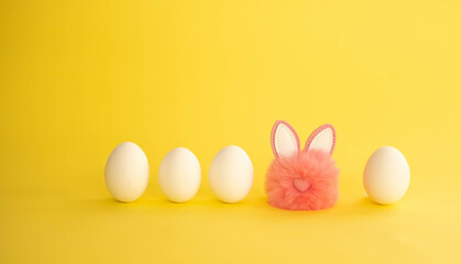 Naklejka na ściany i meble Minimalistic Easter composition. White eggs stand in a row, among them a pink fluffy ball with rabbit ears on a yellow background. I welcome the trendy color concept with copy space.