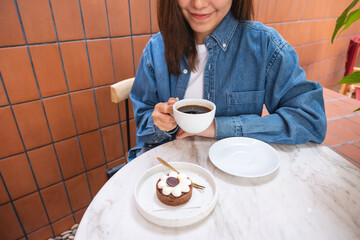 Closeup image of a young woman drinking coffee and eating a chocolate tart in cafe