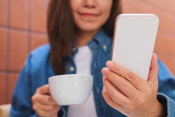 Closeup image of a young woman holding and using mobile phone while drinking coffee in cafe