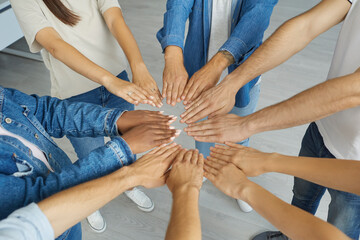 Team of diverse multircial people join hands. Group of different young mixed race people standing in circle and putting their hands together. Cropped high angle closeup shot. Teamwork, union concept