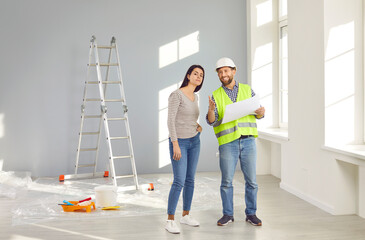 Builder, repairman showing house design plan to apartment owner. Working man in hardhat discussing blueprint of renovation and interior decoration with young woman