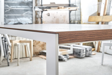 Fototapeta na wymiar Minimalism style dining table with thin wooden table top of toned oak veneer on white metal legs in workshop closeup