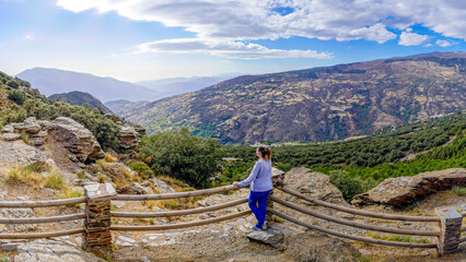Fototapeta na wymiar Pretty young woman dressed in jeans and sweatshirt enjoying the landscape of a valley in the Alpujarra of Granada
