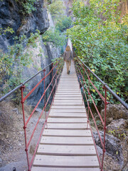 White and blonde young woman walking on a red suspension bridge with wooden planks