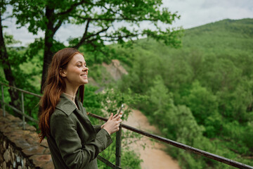 a woman in a raincoat takes pictures on the phone of a beautiful view of the forest. Travel, technology, mobile photography