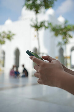 closeup of female hand holding smartphone with mosque background in blur