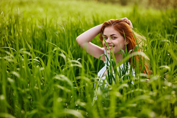 Naklejka na ściany i meble happy woman sitting in tall green grass holding her hair
