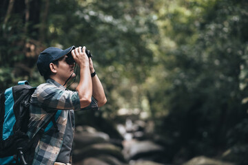 Obraz premium Hikers use binocular to see animals and view landscape with backpacks in the forest. hiking and adventure concept.