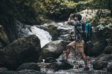 Hikers standing on the rock and use binocular to see animals and view landscape with backpacks and waterfall background in the forest. hiking and adventure concept.