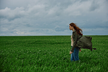 Naklejka na ściany i meble a sad woman in a coat stands in a field in cloudy weather resisting a strong wind