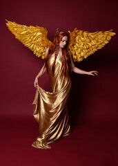 Full length portrait of beautiful woman model with long red hair, gold silk robes, crown & fantasy...