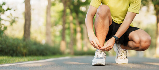 Young athlete man tying running shoes in the park outdoor, male runner ready for jogging on the road outside, asian Fitness walking and exercise on footpath in morning. wellness and sport concepts - obrazy, fototapety, plakaty
