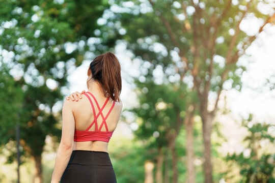 Young fitness woman holding her sports injury shoulder and neck, muscle painful during training. Asian runner female having body problem after exercise outside in summer