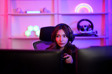 Obraz na płótnie Canvas Asian young gamer girl watching and thinking about strategy game before clear to the next stage level in neon entertainment room