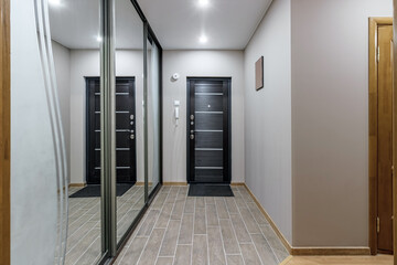 long corridor in interior of entrance hall of modern apartments with doors, cabinets, shelves and a mirror