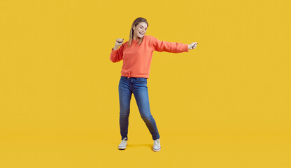 Fototapeta na wymiar Overjoyed young woman isolated on yellow studio background dance enjoy music. Smiling millennial Caucasian girl have fun show dancer movements. Hobby and entertainment.