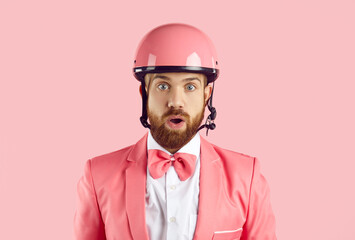 Headshot of young man with ginger beard, wearing modern pink bike helmet, stylish funky suit and bowtie looking at you with open mouth and funny surprised, shocked, stunned or scared facial expression
