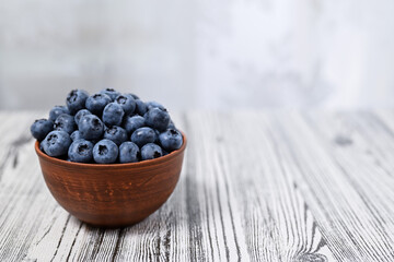 Fresh organic blueberries in a clay bowl. Light wooden background, shallow depth of field, copy...