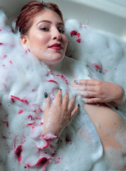 beautiful red-haired woman, with a beautiful look celebrating love with rose petals in the bathtub, woman in the tub with foam and rose petals, red lips like crimson, semi-naked woman in the jacuzzi