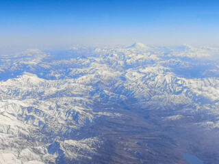 Snowy mountains with clouds as background. View from the airplane window.