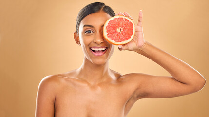 Face smile, skincare and woman with grapefruit in studio isolated on a brown background. Portrait, natural cosmetics and happy Indian female model with citrus fruit for vitamin c, nutrition or beauty